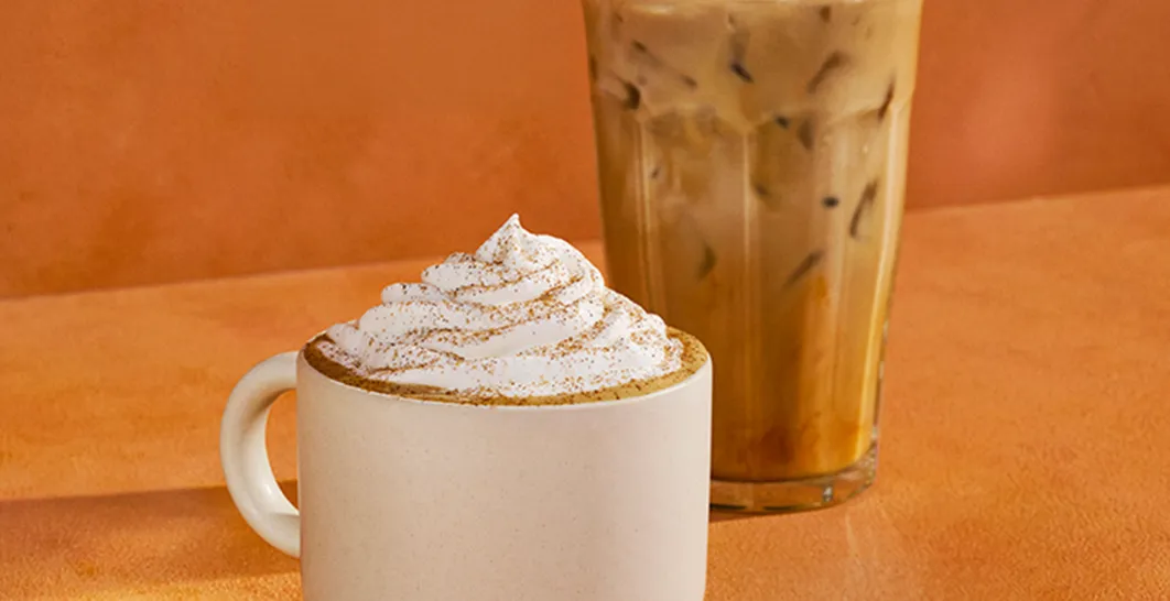 Starbucks Pumpkin Spice Latte in a white mug topped with whipped cream and pumpkin spice, with an iced Pumpkin Spice Latte in a clear glass behind it on an orange background.